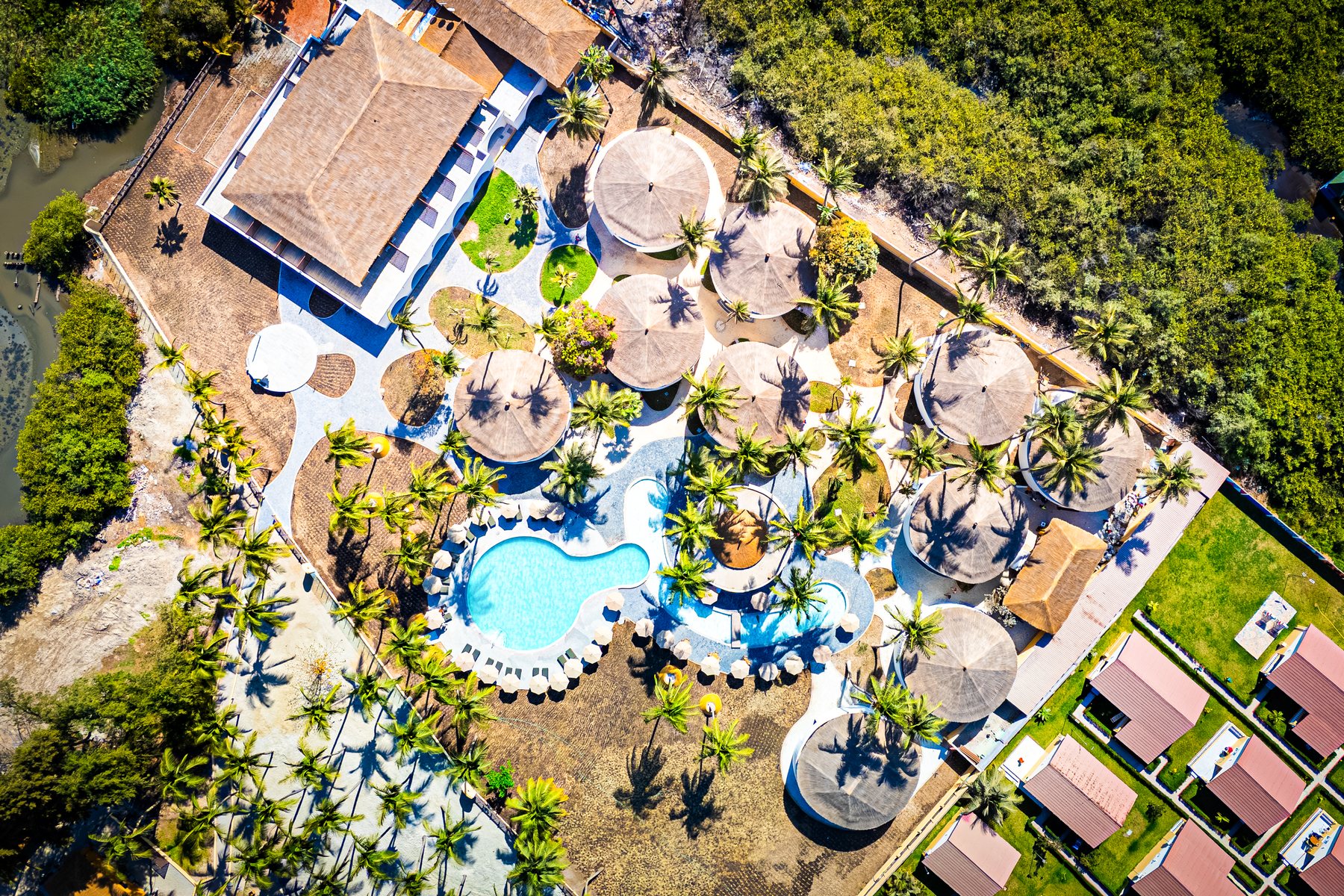 Aerial view of Palm Beach Resort in Kotu, showing round thatched buildings, palms and the resort swimming pool
